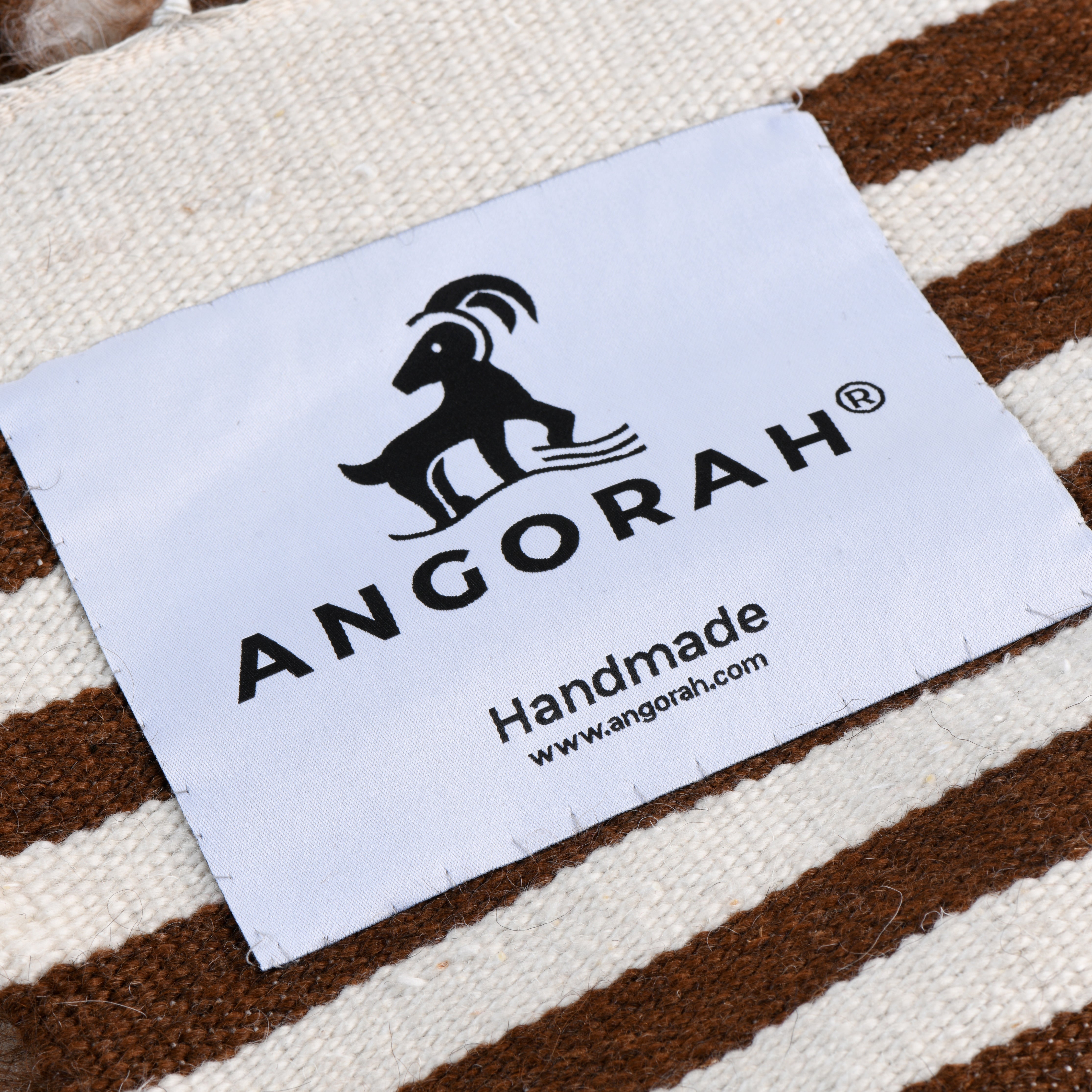 Close-up of the Agate handcrafted natural mohair striped rug featuring the Angorah branding label, showcasing organic wool in brown and cream stripes.