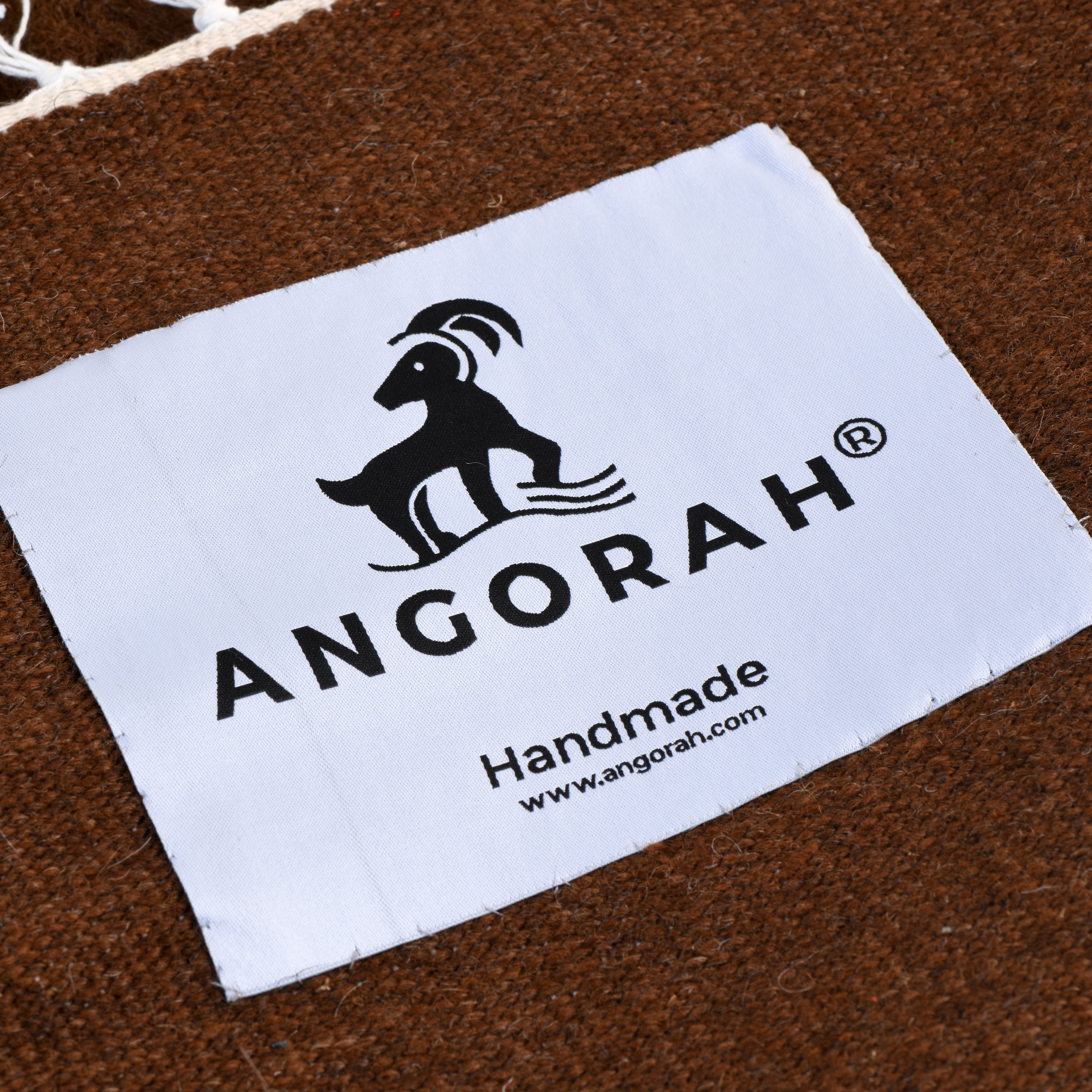 Close-up of the Angorah label on the Sjakkmatt organic mohair rug, highlighting the handcrafted quality and chessboard-inspired design in earthy browns and soft whites