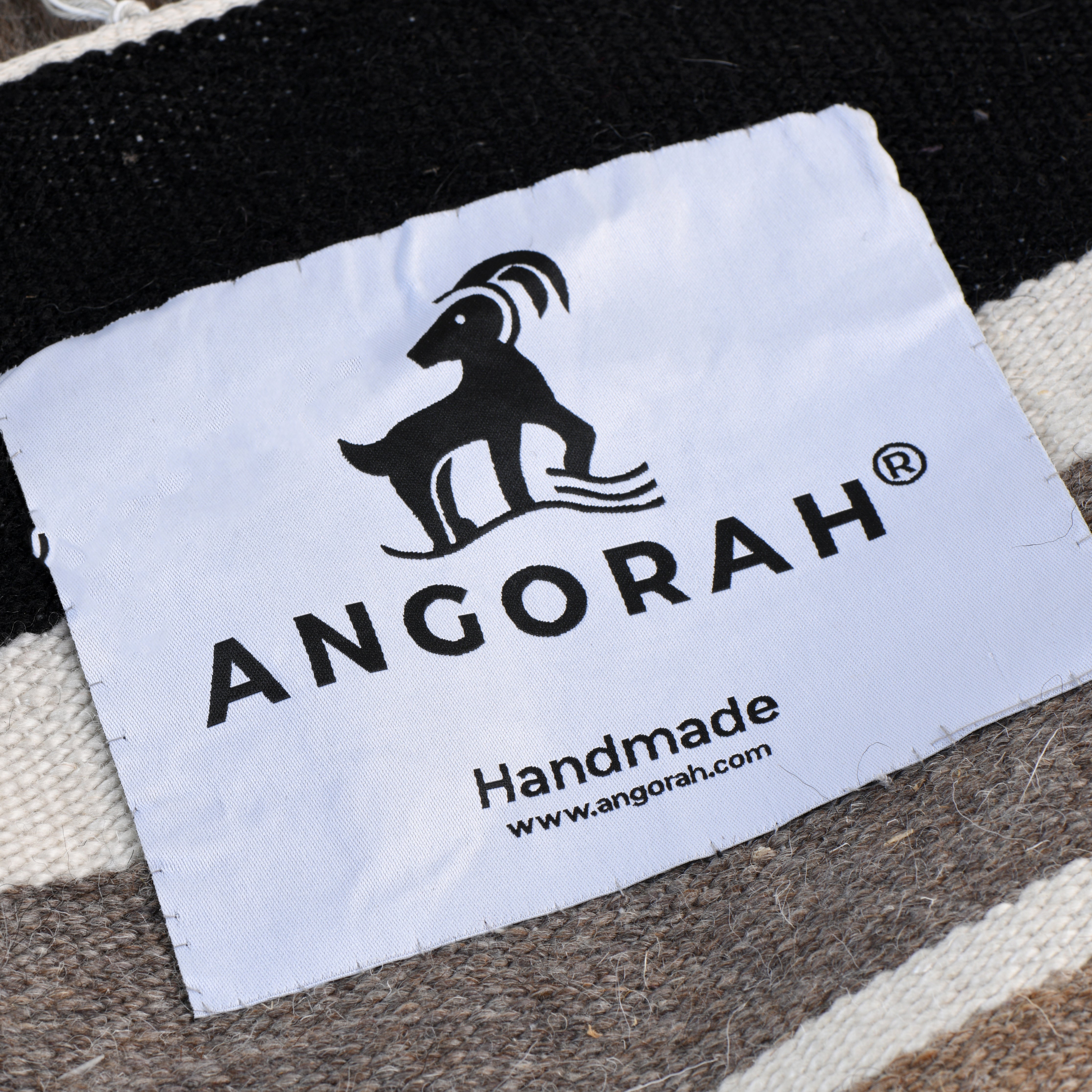 Close-up view of the Angorah label on the Kurozumiya handmade rug, crafted from 100% organic natural mohair sourced from Angora goats. This image highlights the artisan quality and craftsmanship of the Scandinavian design rug, reflecting its luxurious softness and durability.