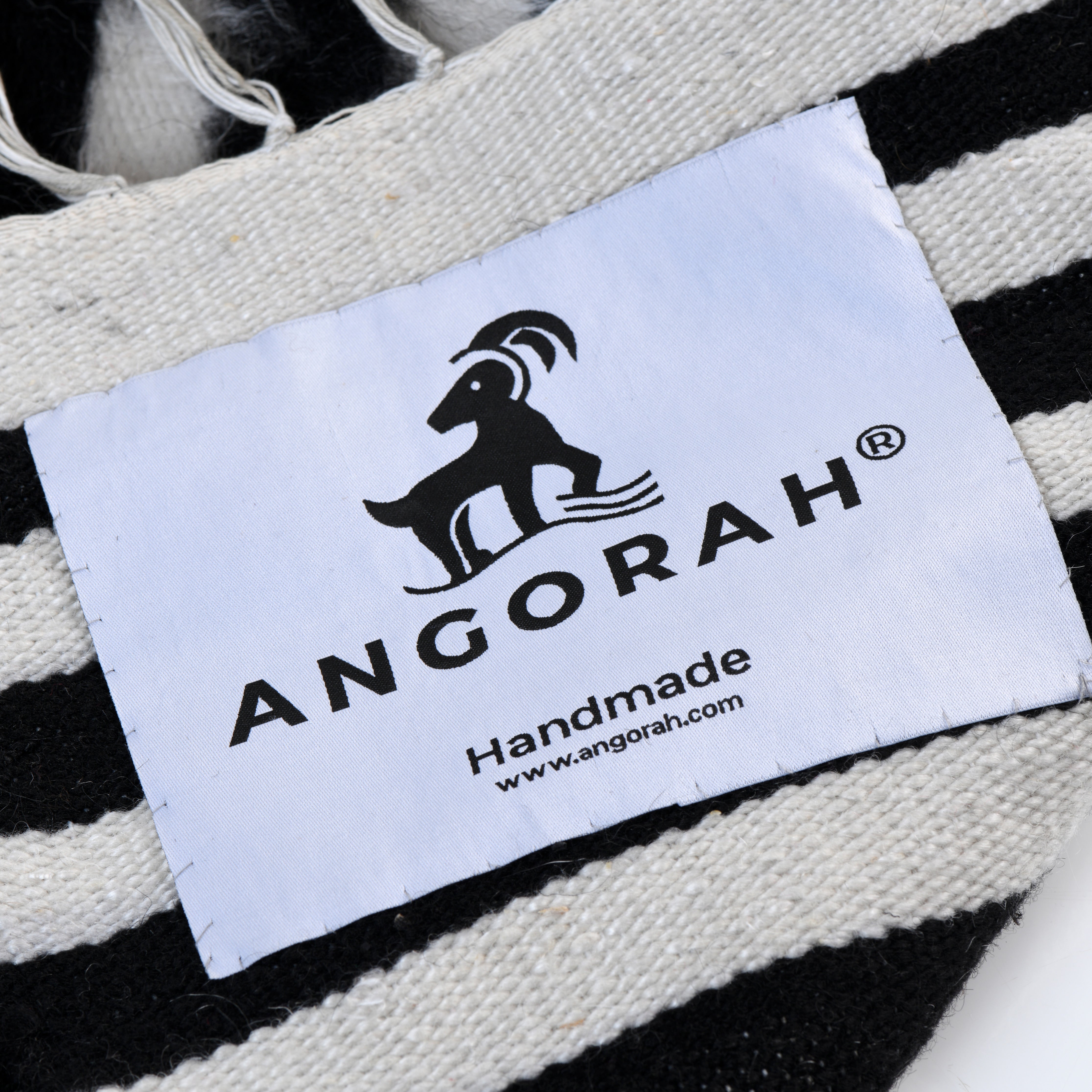 Close-up of the Angorah brand label on the Sleipnir handcrafted rug, made from 100% organic natural mohair. The label, featuring the Angorah logo, highlights the rug's handmade quality and authentic craftsmanship, symbolizing luxury and sustainable production.